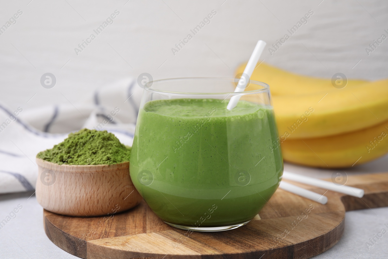 Photo of Glass of tasty matcha smoothie and powder on light table