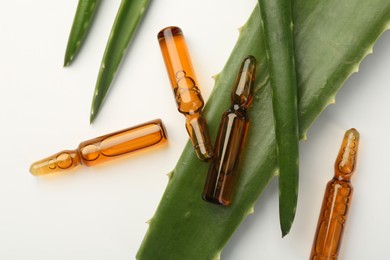 Skincare ampoules and aloe leaves on white background, flat lay