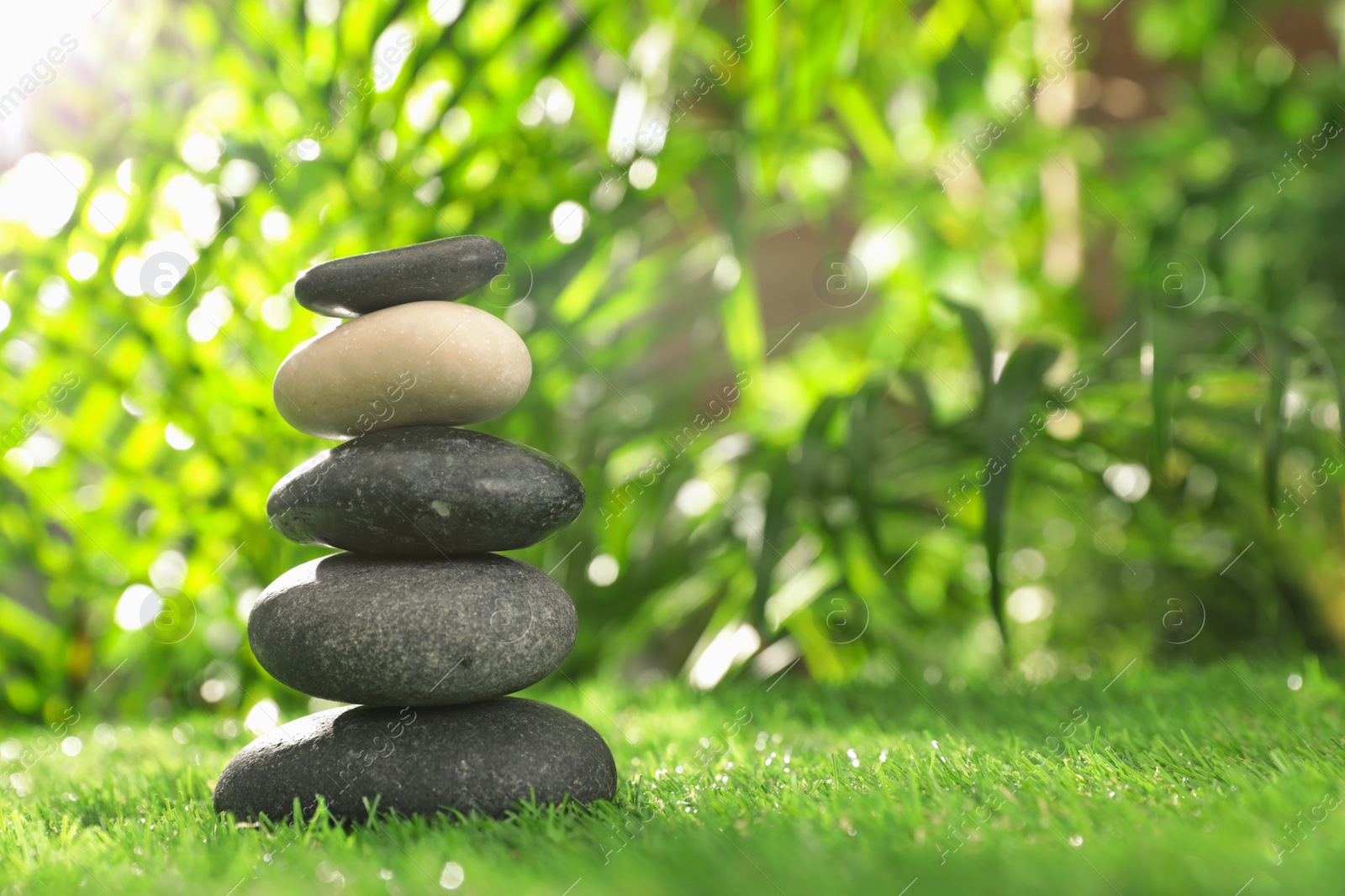 Photo of Stack of stones on green grass against blurred background, space for text. Zen concept