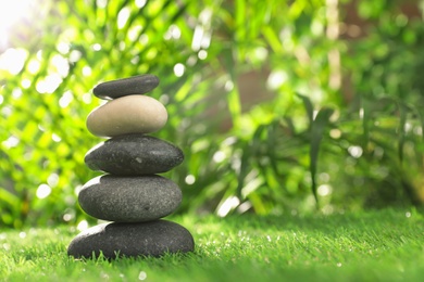 Photo of Stack of stones on green grass against blurred background, space for text. Zen concept