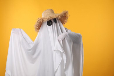 Photo of Person in ghost costume and straw hat on yellow background