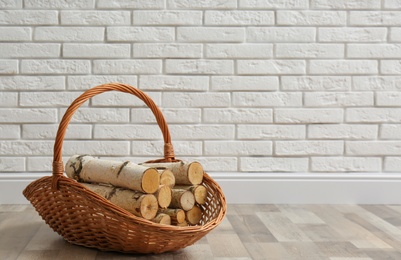 Photo of Wicker basket with firewood near white brick wall indoors, space for text