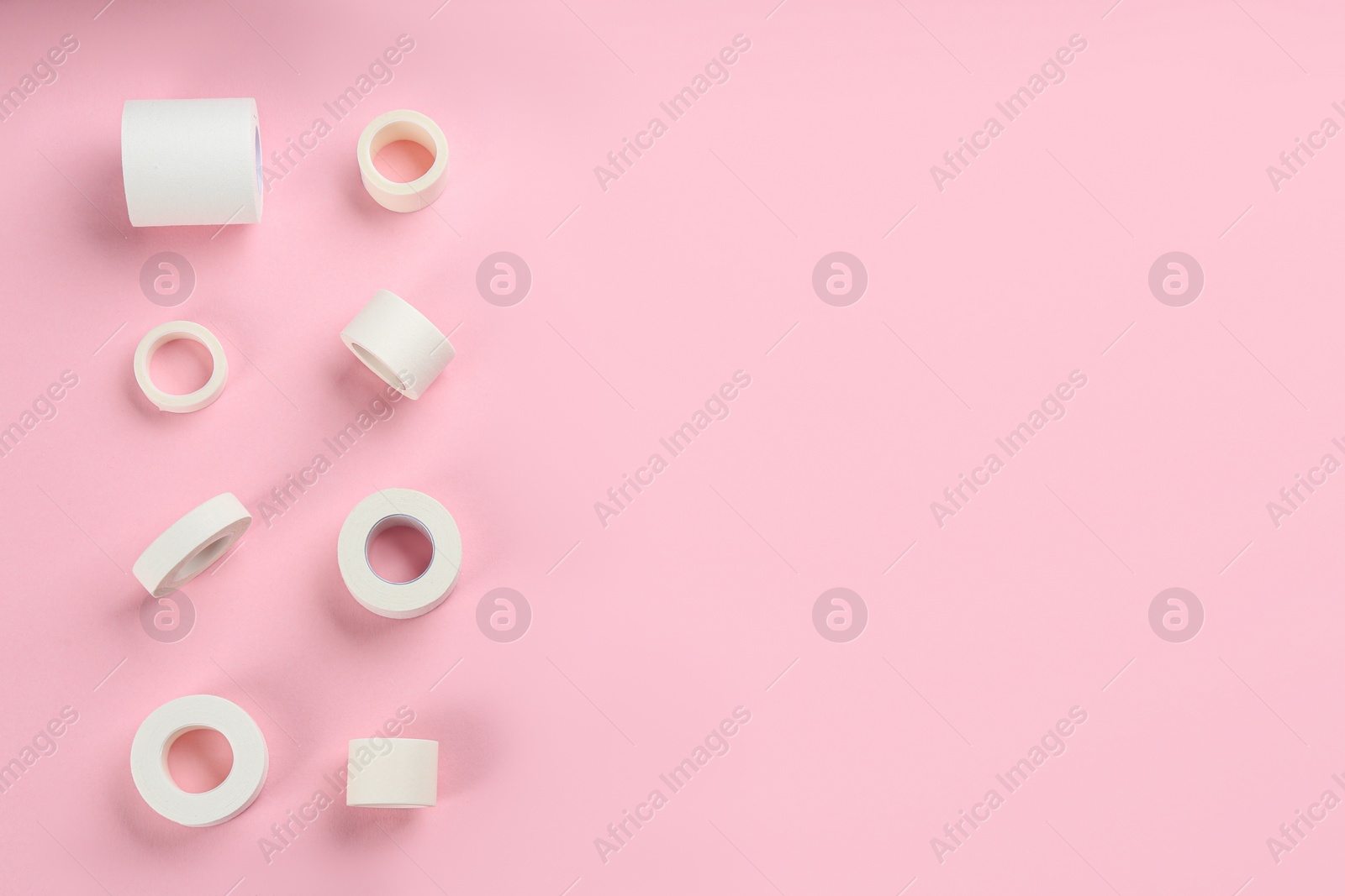 Photo of Sticking plaster rolls on pink background, flat lay. Space for text