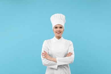Photo of Happy female chef wearing uniform and cap on light blue background