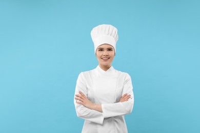 Happy female chef wearing uniform and cap on light blue background