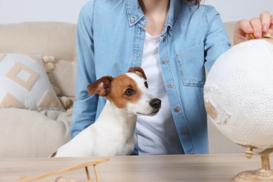 Photo of Woman pointing at globe near dog indoors, closeup. Travel with pet concept