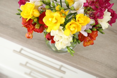 Photo of Beautiful spring freesia flowers on chest of drawers, closeup