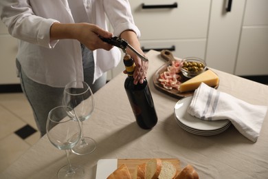 Photo of Woman opening wine bottle with corkscrew at table indoors, closeup