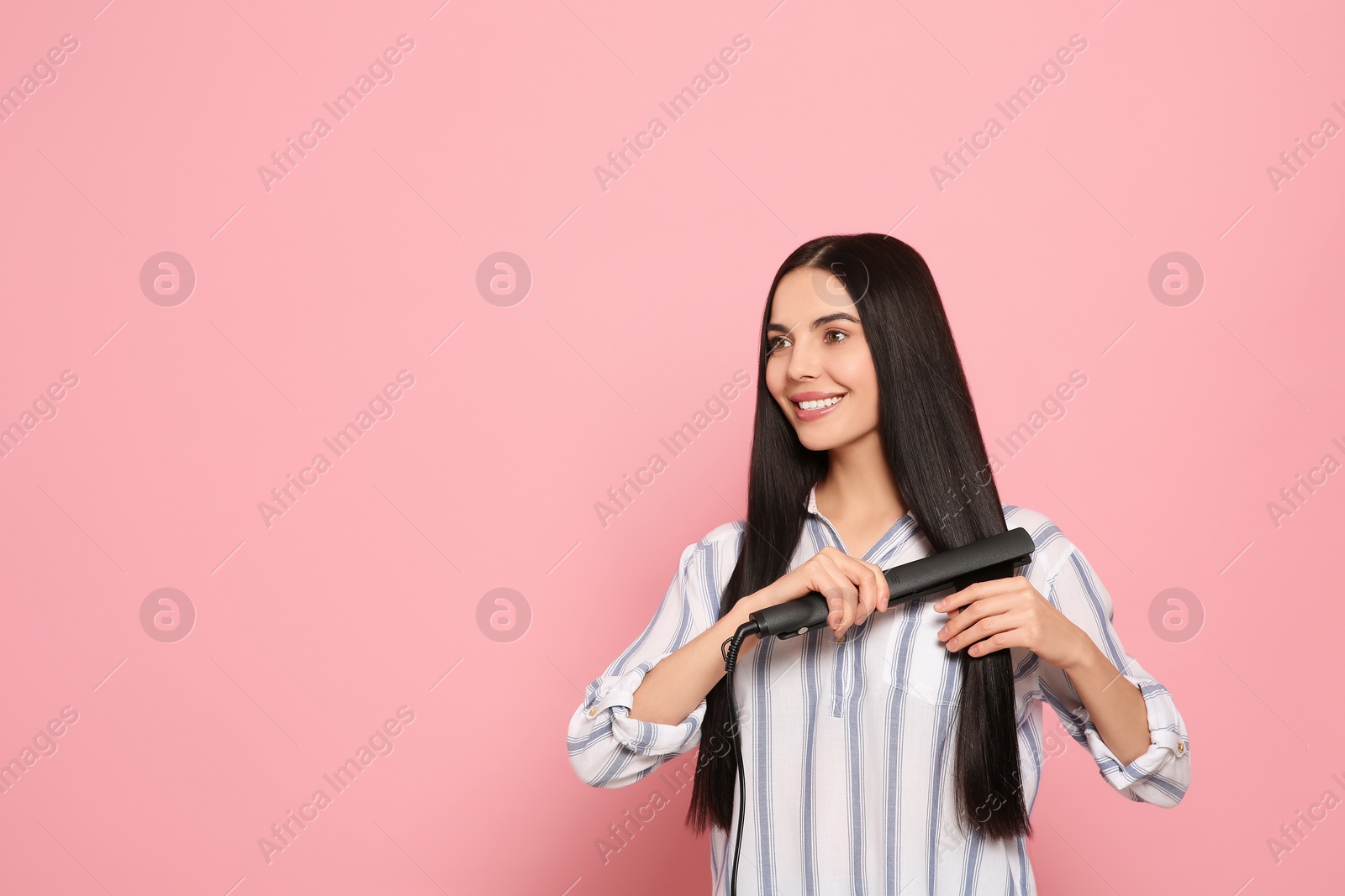 Photo of Beautiful happy woman using hair iron on pink background. Space for text