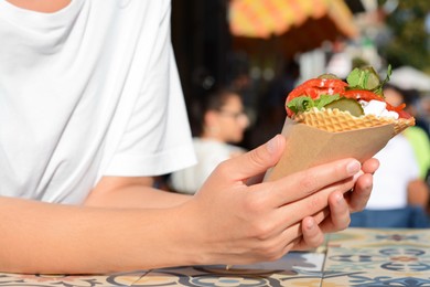 Photo of Woman holding wafer with falafel and vegetables at colorful tiled table outdoors, closeup. Street food
