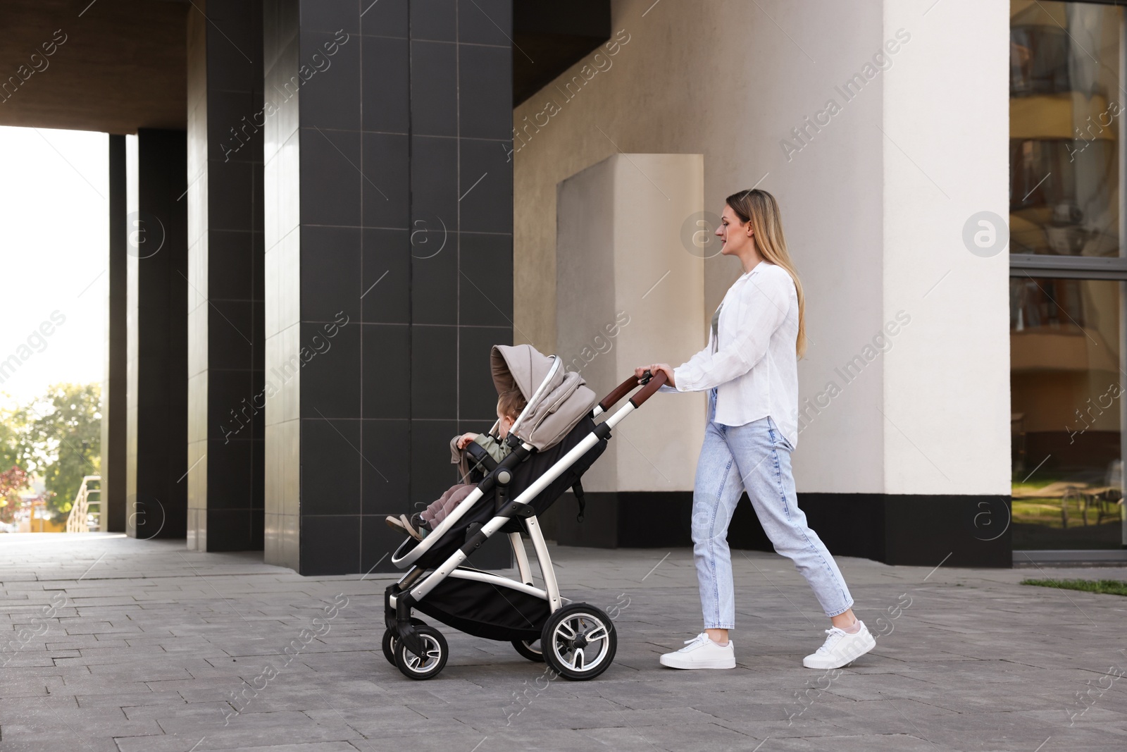 Photo of Nanny with cute little boy in stroller walking outdoors