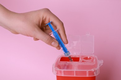 Photo of Woman throwing used syringe into sharps container  on pink background, closeup