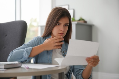 Worried woman reading paper letter at home