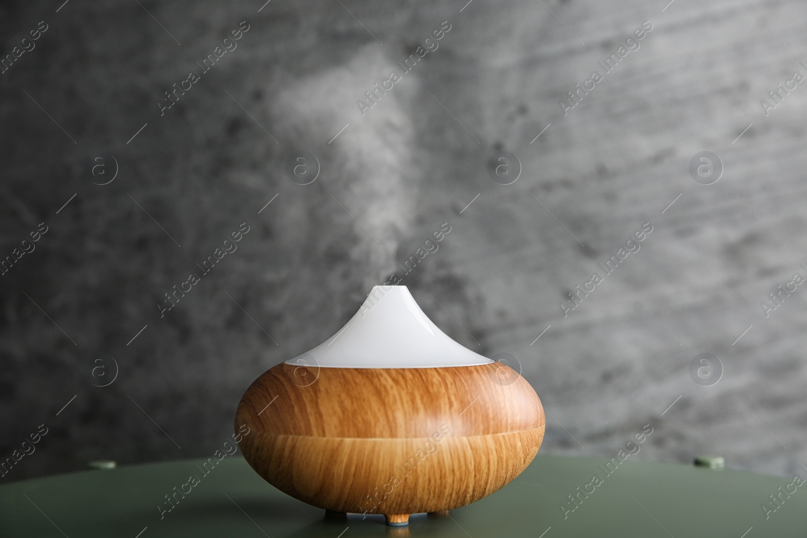 Photo of Modern essential oil diffuser on green table against dark grey background