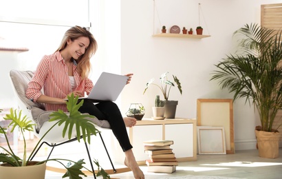 Photo of Young woman using laptop at home, space for text. Trendy room interior with plants