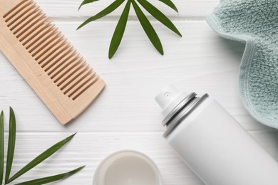 Photo of Dry shampoo spray, comb, towel and green twigs on white wooden table, flat lay
