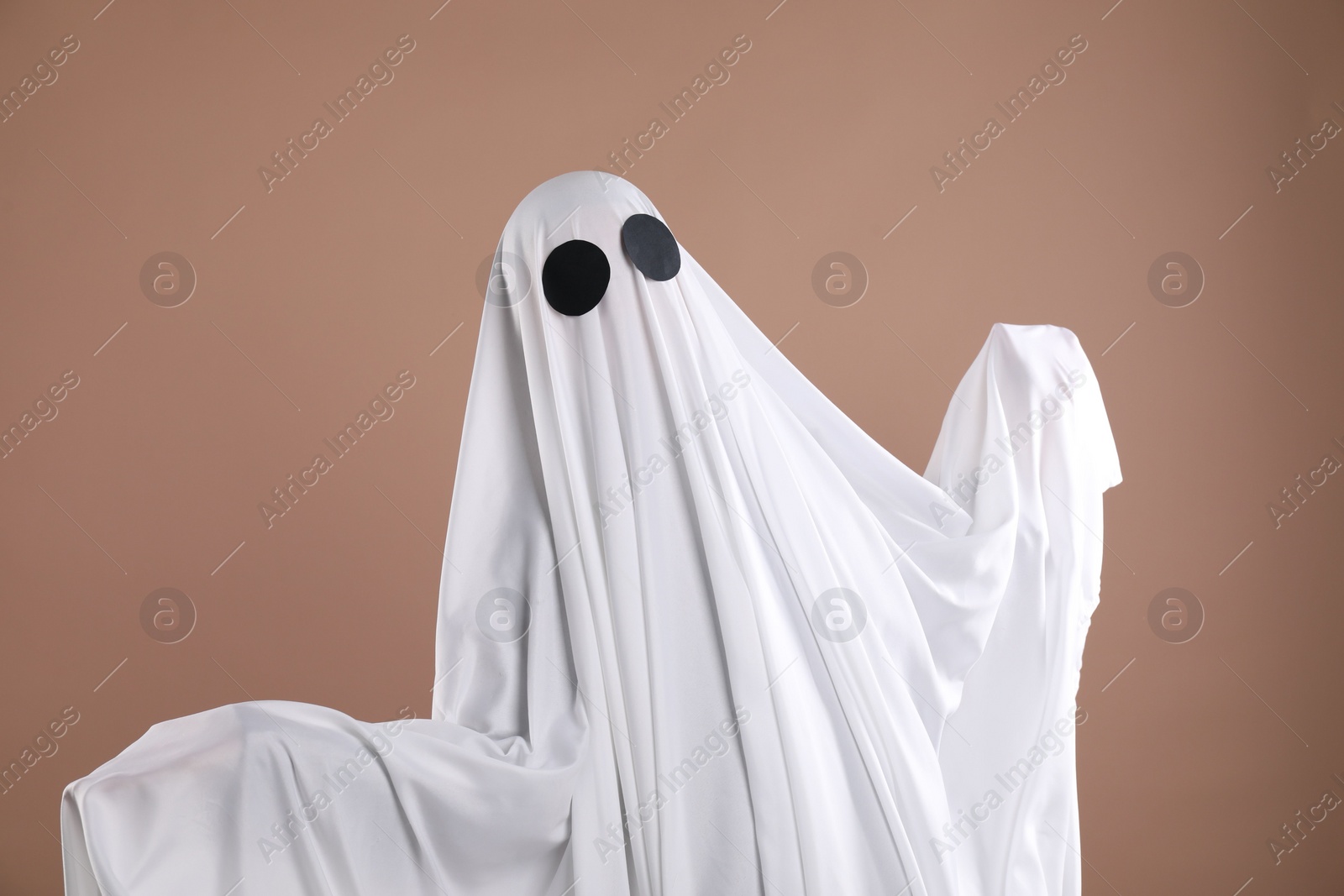 Photo of Creepy ghost. Person covered with white sheet on dark beige background