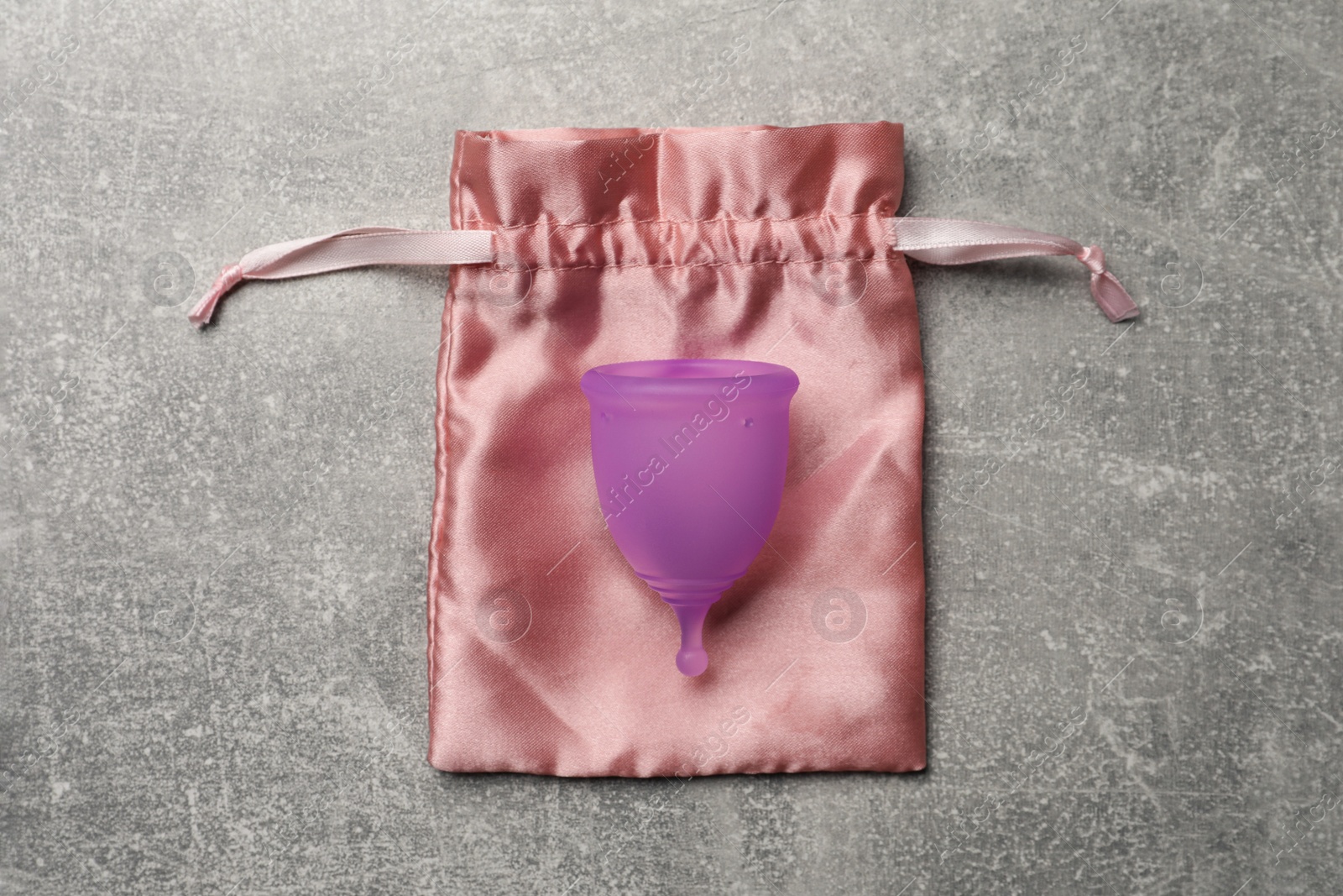 Photo of Menstrual cup and cotton bag on grey background, top view. Reusable feminine hygiene product