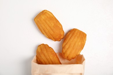 Photo of Paper bag with delicious madeleine cakes on white background, flat lay