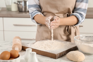 Photo of Woman sprinkling flour over board on table in kitchen