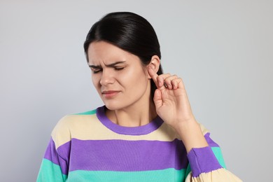 Photo of Young woman suffering from ear pain on light grey background