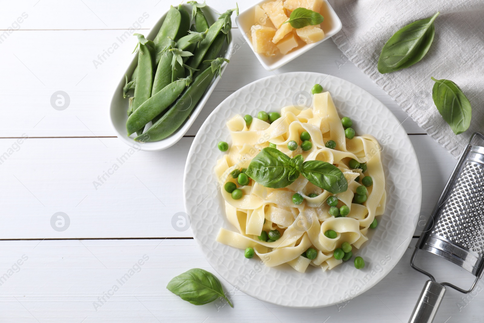 Photo of Delicious pasta with green peas and fresh basil on white wooden table, flat lay. Space for text