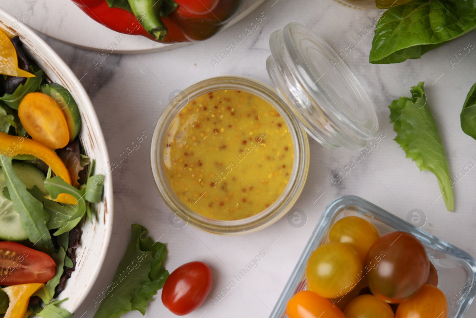 Photo of Tasty vinegar based sauce (Vinaigrette) in jar, salad and products on white marble table, flat lay