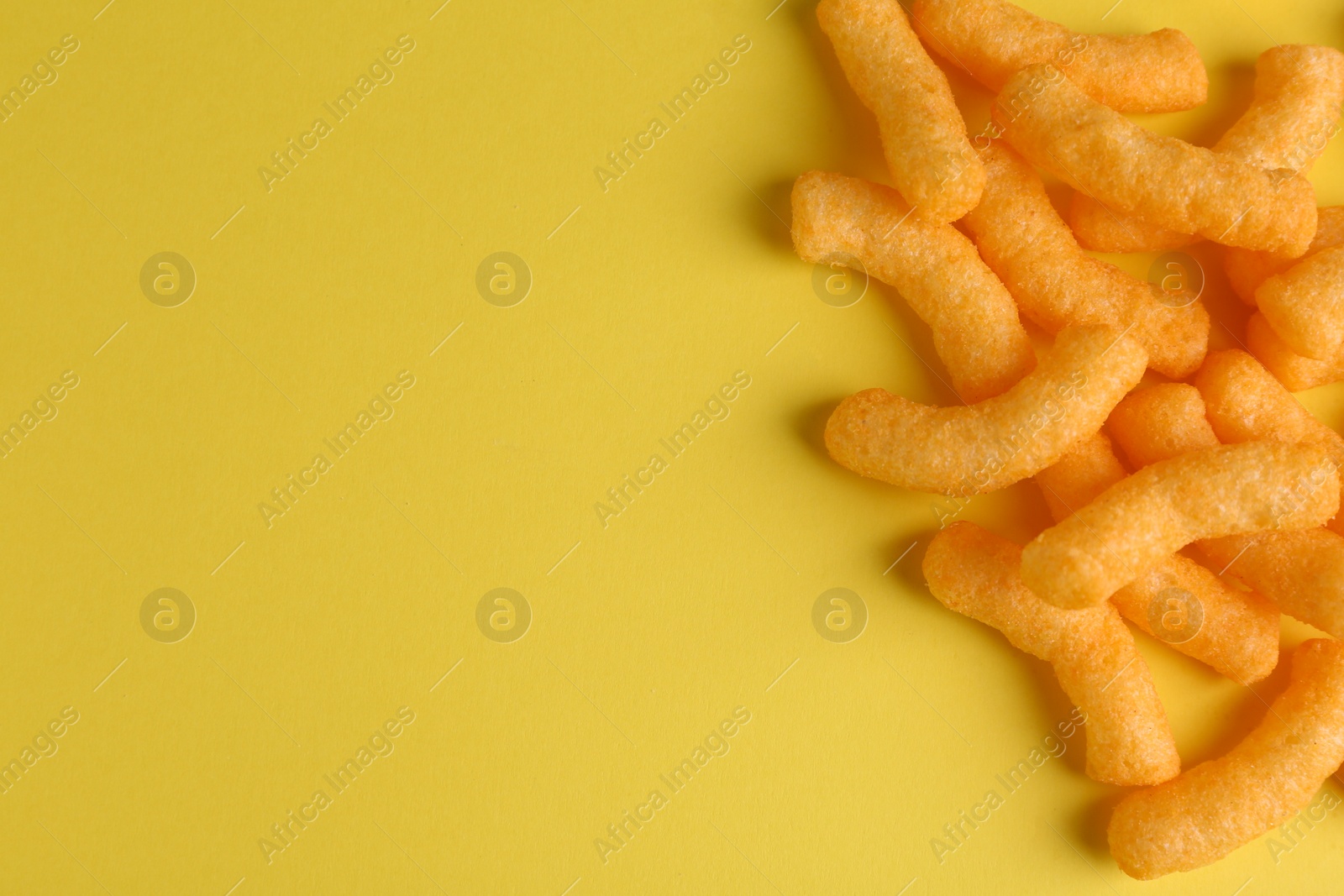 Photo of Tasty cheesy corn puffs on yellow background, flat lay. Space for text