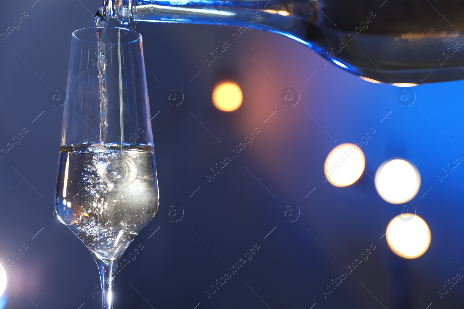 Photo of Champagne pouring from bottle into glass on color background, closeup. Space for text