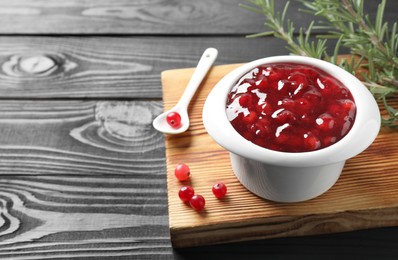 Photo of Cranberry sauce in bowl, fresh berries, spoon and rosemary on black wooden table, closeup. Space for text