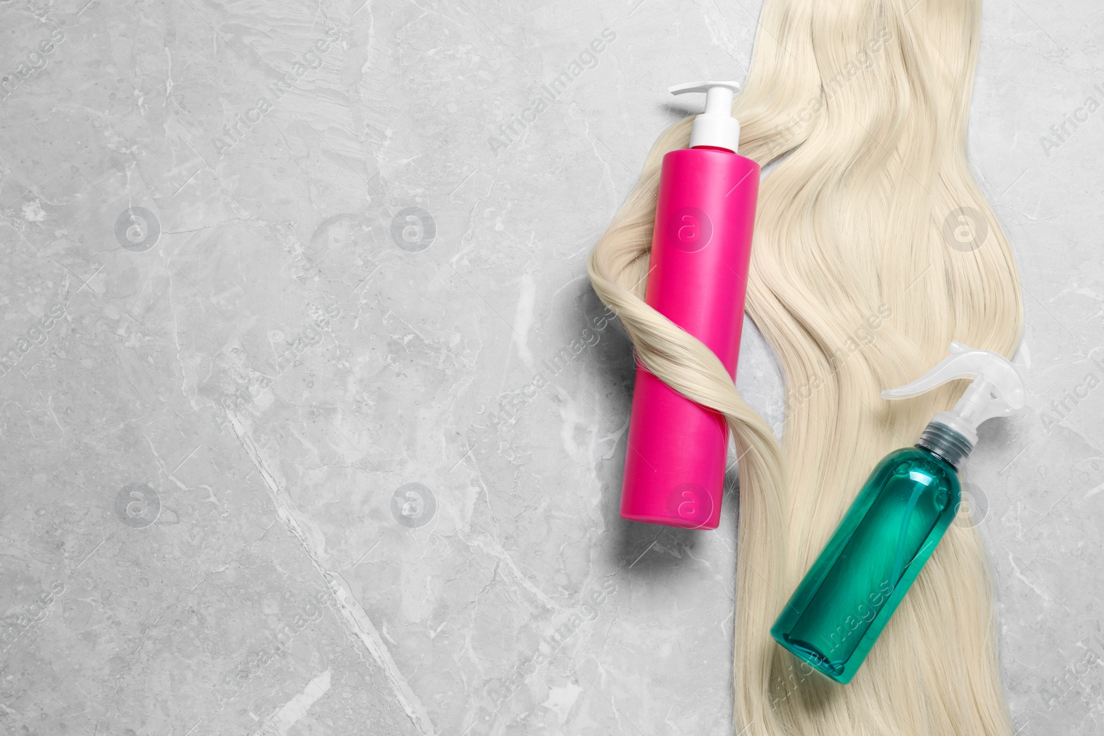 Photo of Spray bottles with thermal protection and lock of blonde hair on grey marble table, flat lay. Space for text