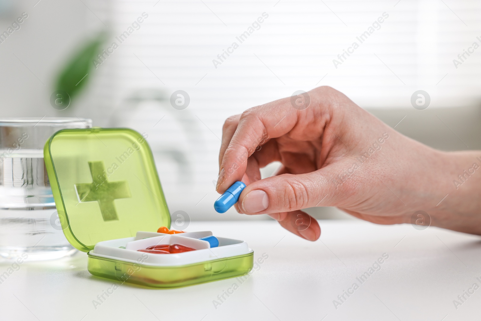 Photo of Woman with pills, organizer and glass of water at white table, closeup