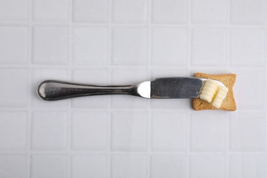 Tasty butter curl, knife and piece of dry bread on white tiled table, top view