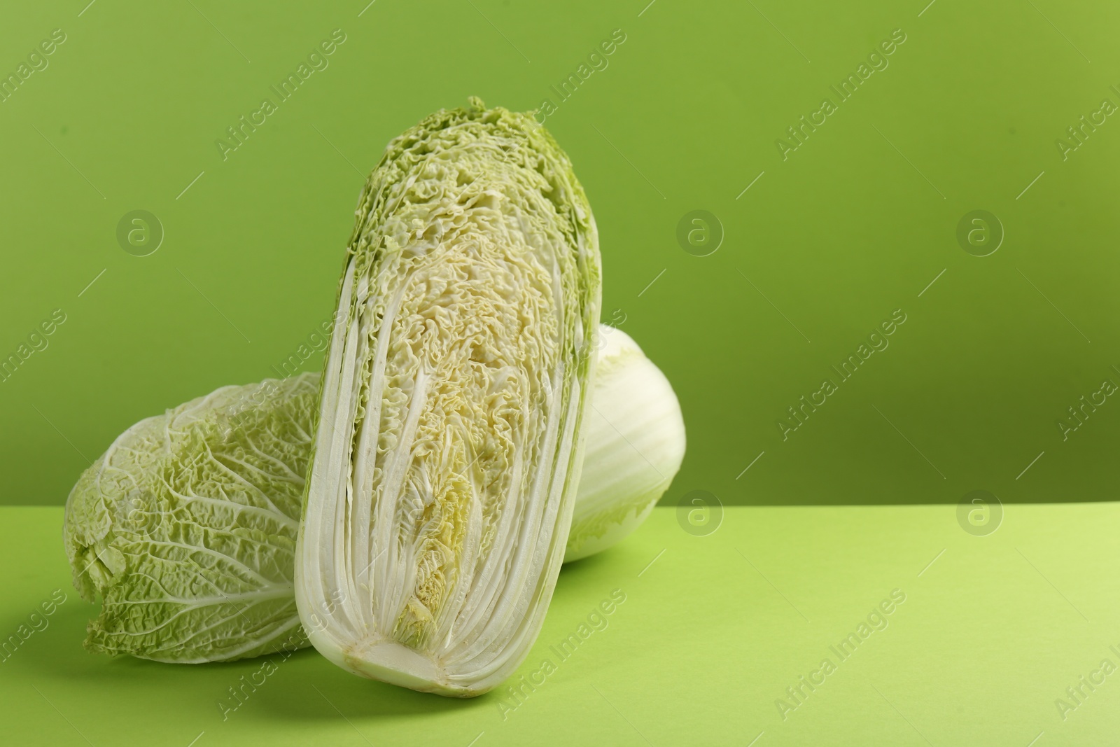 Photo of Whole and cut fresh Chinese cabbage on light green background. Space for text