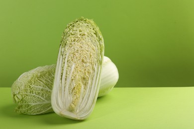 Photo of Whole and cut fresh Chinese cabbage on light green background. Space for text