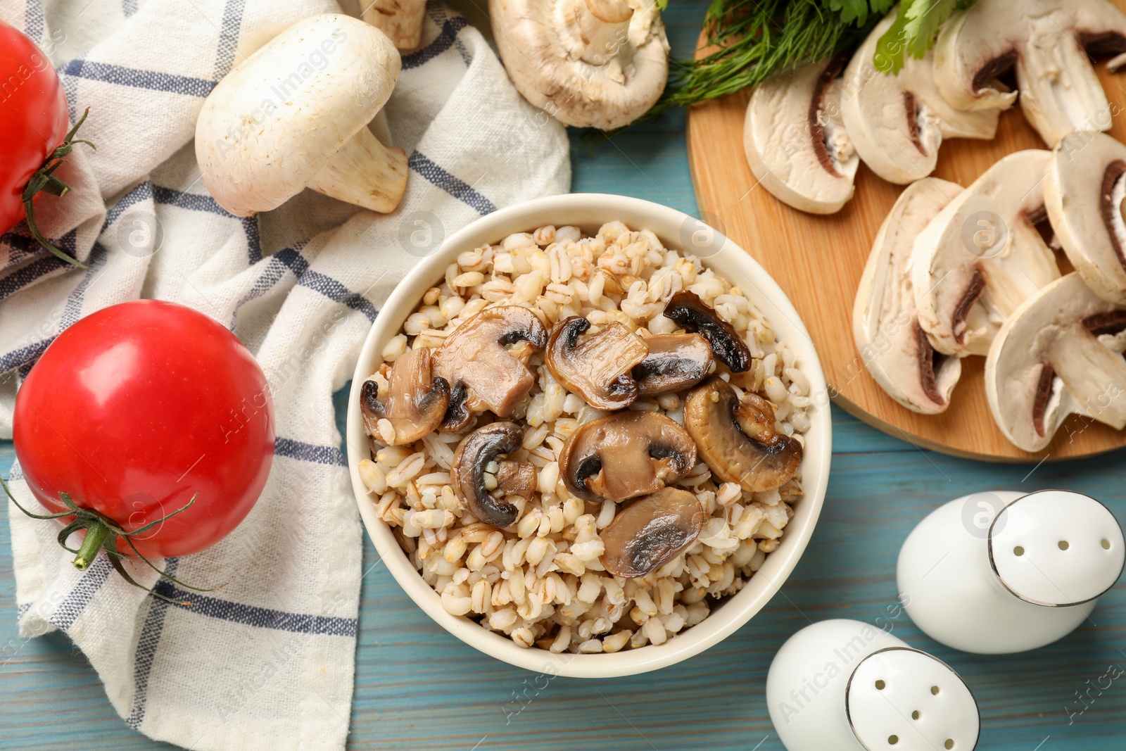 Photo of Delicious pearl barley in bowl served on light blue wooden table, flat lay