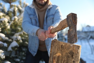 Photo of Man chopping wood with axe outdoors on winter day, closeup