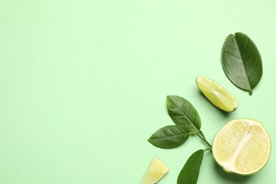 Photo of Cut fresh ripe limes with leaves on light green background, flat lay