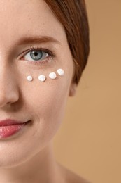 Beautiful woman with freckles and cream on her face against beige background, closeup