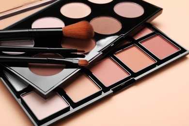 Photo of Colorful contouring palettes with brushes on beige background, closeup. Professional cosmetic product