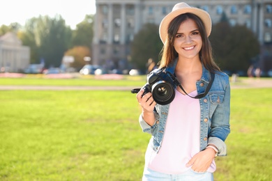 Photo of Young female photographer holding professional camera on street. Space for text