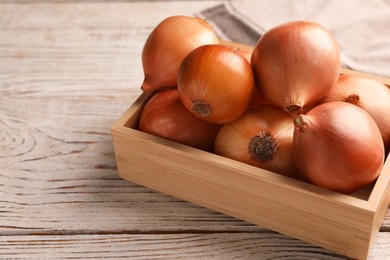 Crate with ripe onions on white wooden table, closeup. Space for text