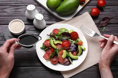 Woman adding soy sauce to tasty salad at wooden table, above view