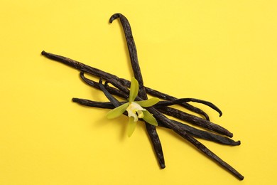 Photo of Vanilla pods and beautiful flower on yellow background, top view
