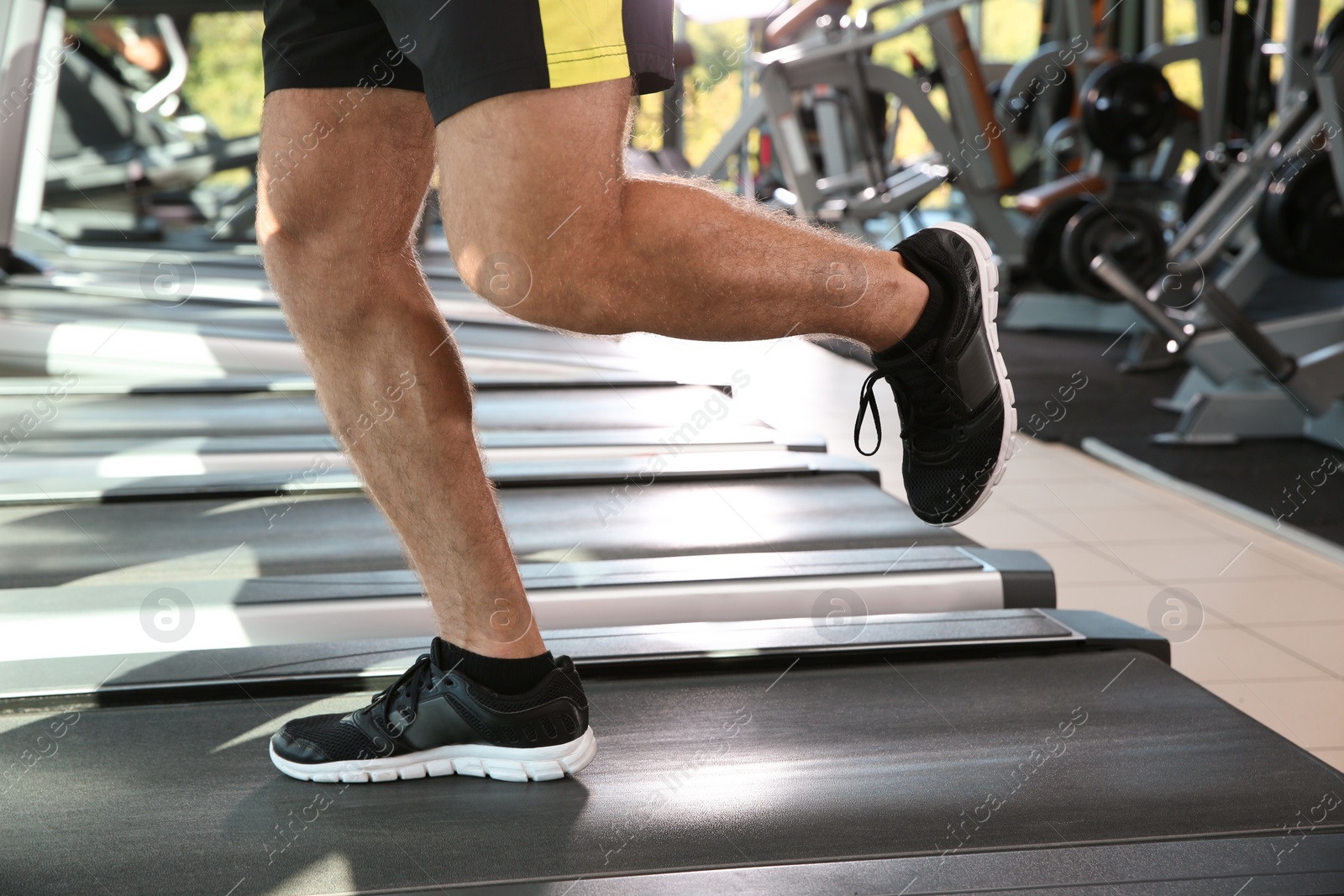 Photo of Strong young man on treadmill in gym, closeup of legs