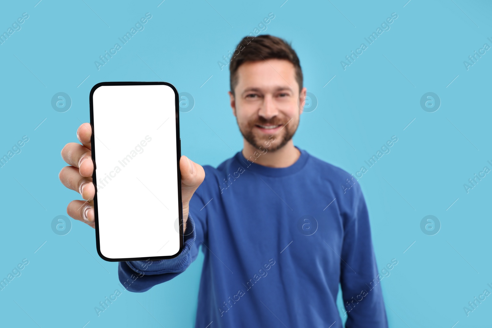 Photo of Handsome man showing smartphone in hand on light blue background, selective focus. Mockup for design