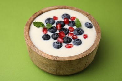 Photo of Bowl of delicious semolina pudding with blueberries, pomegranate and mint on green background, closeup