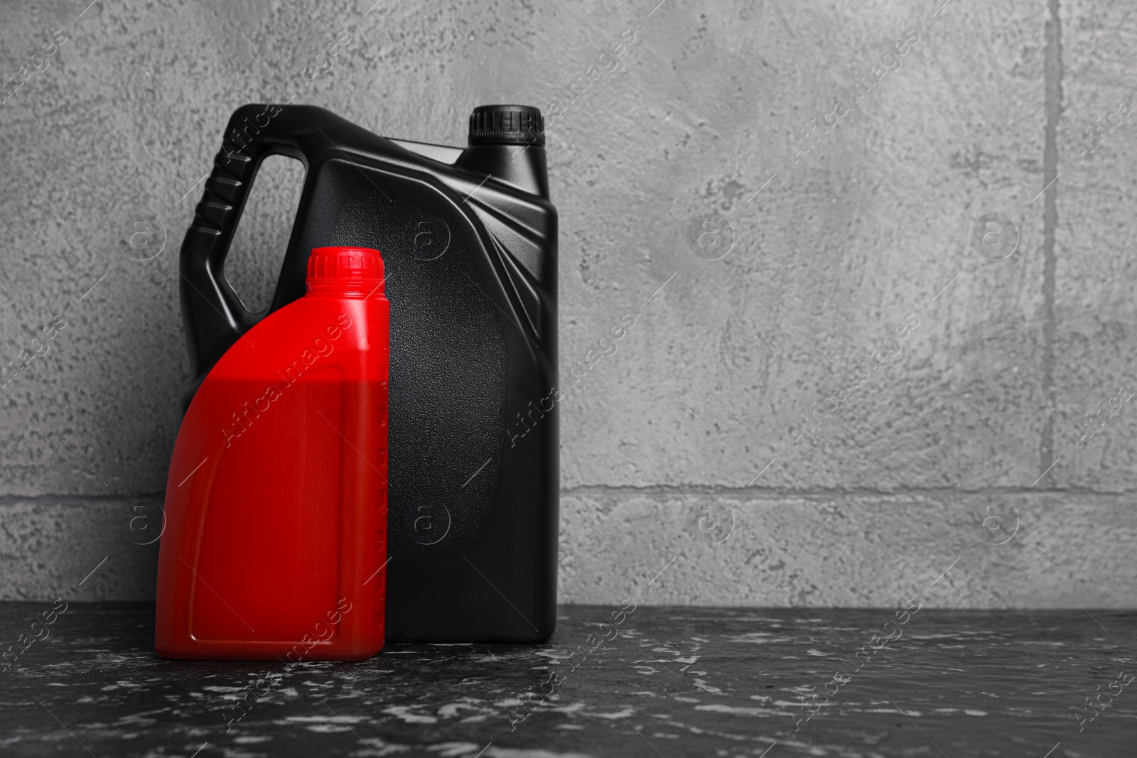 Photo of Motor oil in different canisters on black table near grey wall, space for text