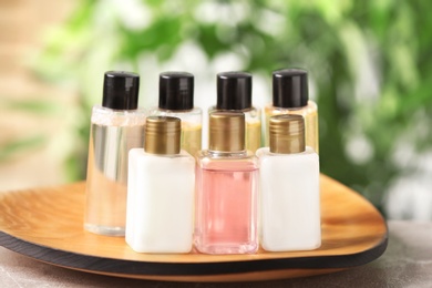 Photo of Mini bottles with cosmetic products on tray against blurred background, closeup. Hotel amenities