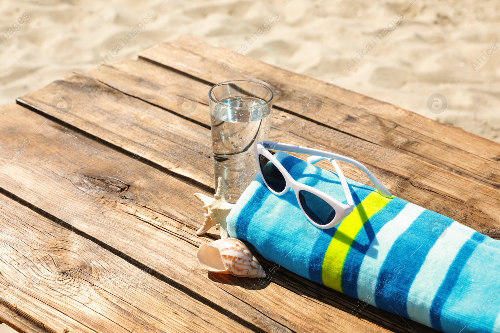 Photo of Wooden deck with glass of refreshing drink and beach accessories on hot summer day